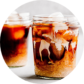 Two jars of cold brew coffee with ice with cream dripping down the insides of the glasses