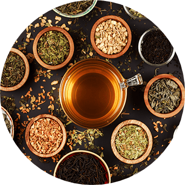 Overhead shot of a glass of black tea with several small bowls of dry tea leaves surrounding the cup