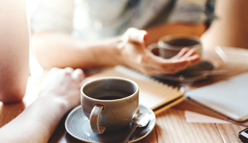 A table with two people, each with a cup and saucer