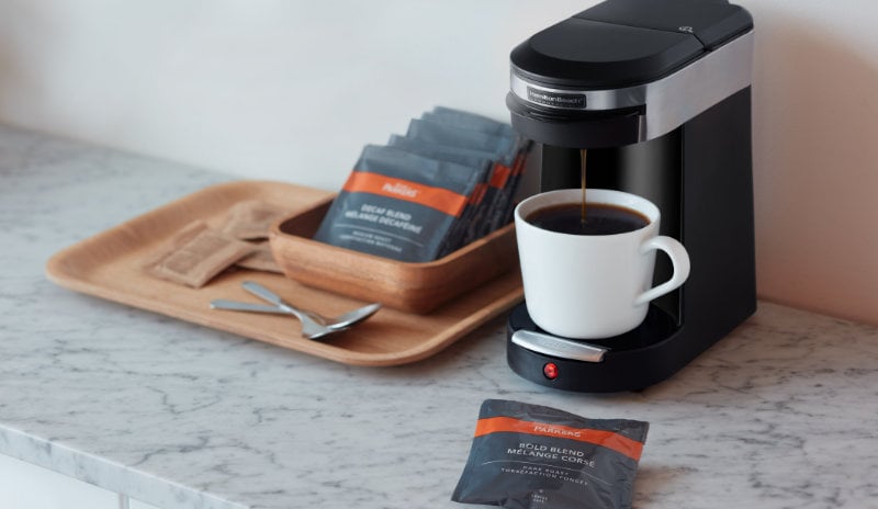 Small coffee brewing machine with a set up of individual coffee pouches, brewing a cup