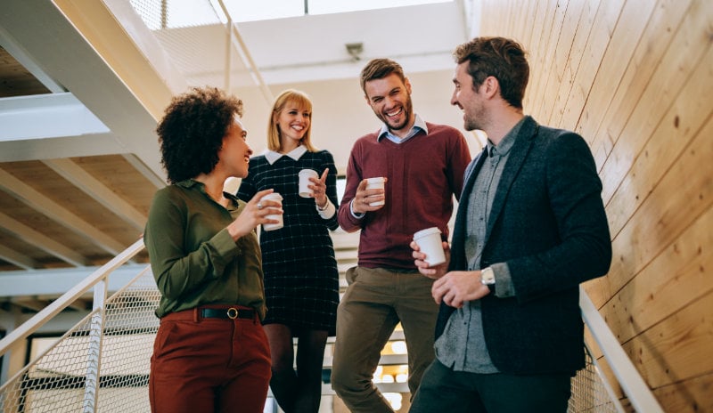 Four people chatting in the stairwell of an office, each with a to-go cup in their hand